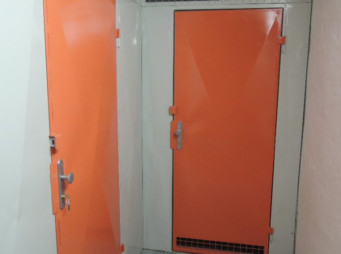 Sklepní kóje ve variantě KOMBI PLECH, odvětrávací mřížka ve spodní části dveří, povrchová úprava – lak (dveře oranžové RAL 2008 a konstrukce šedá RAL 7035), zamykání na FAB, kování klika-koule a jedny očka na visací zámek s bezpečnostní krytkou